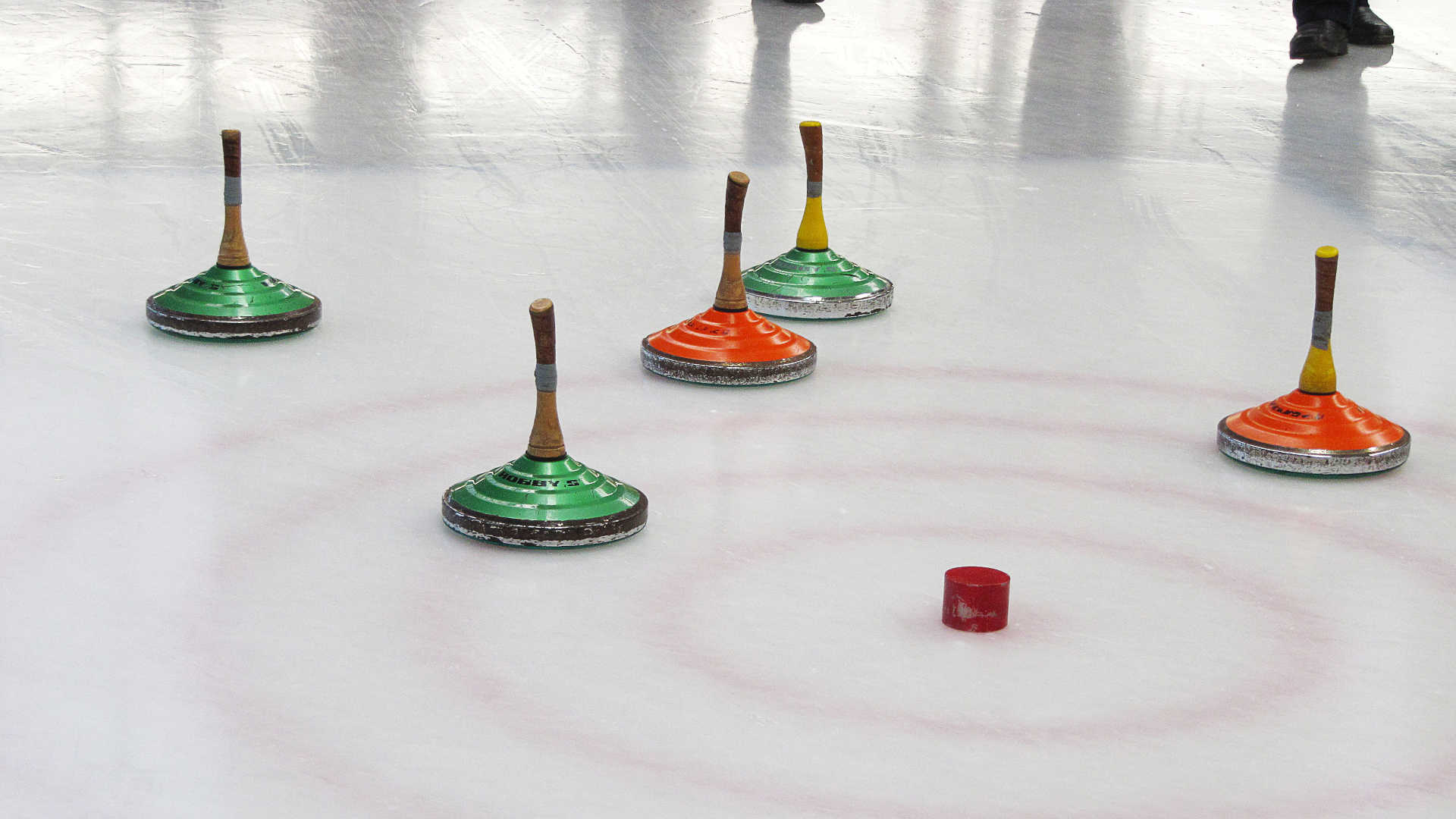 Zwei grüne und zwei orange-farbene Eisstöcke liegen an den Zielkreisen in der Nähe der roten Daube.
