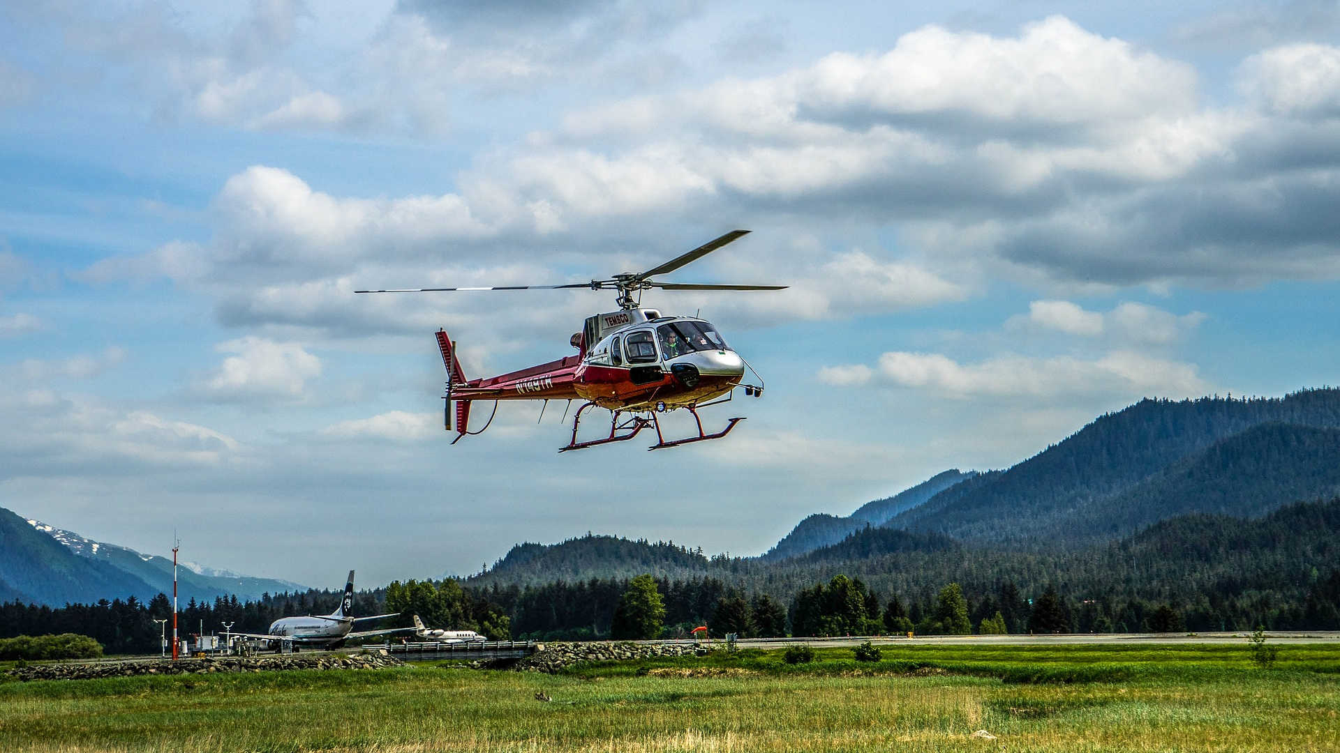 Ein kleiner Flugplatz zwischen den Bergen. Ein rot-silberfarbener Hubschrauber setzt zur Landung an.