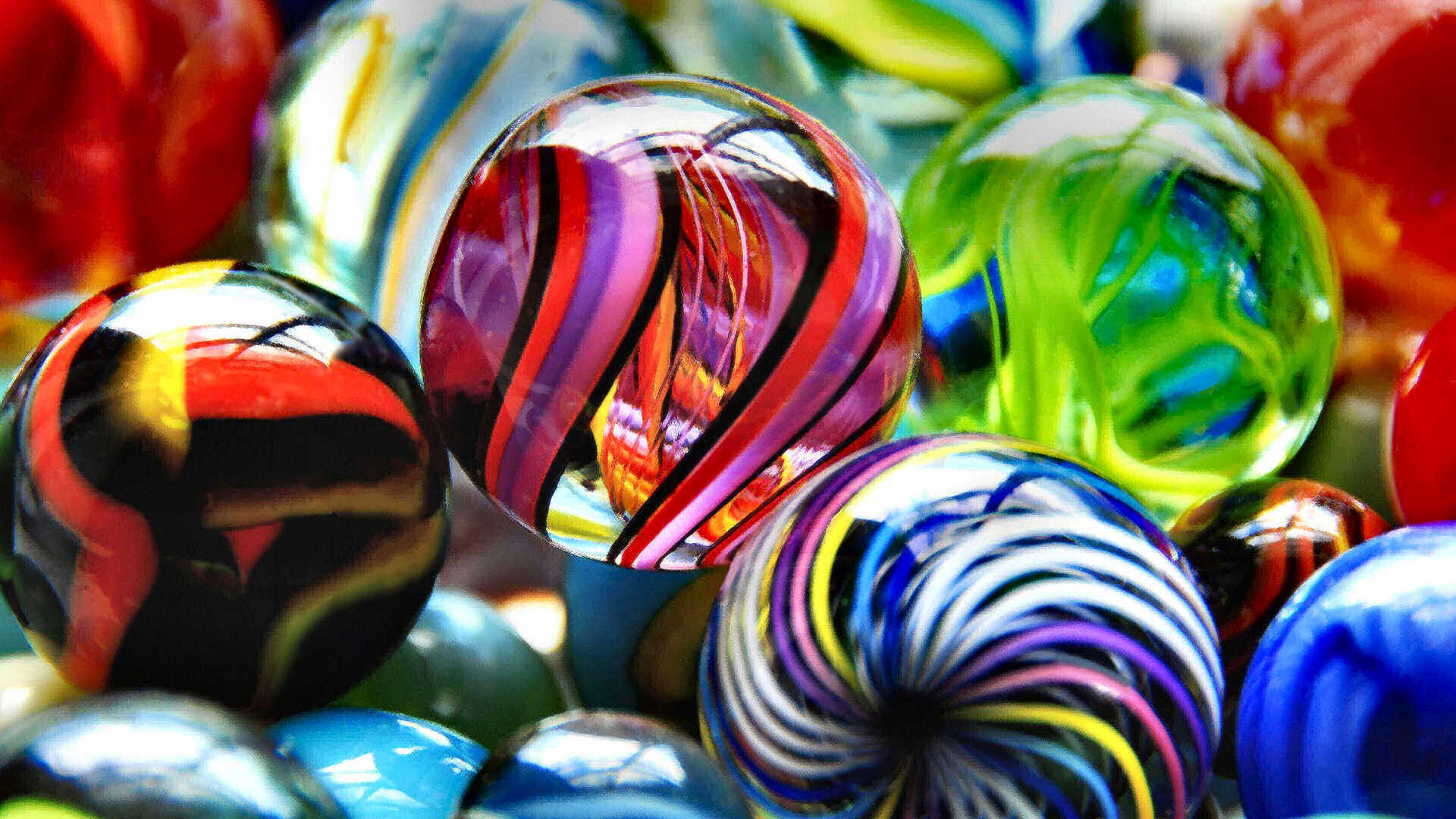 Wir sehen einen kleinen Ausschnitt aus einer Sammlung von wunderschönen Glasmurmeln. Sie strahlen in tollen Farben und spiralförmigen Mustern. Man verspürt den Wunsch, eine davon in die Hand zu nehmen.