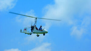 In einem Gyrocopter-Doppelsitzer sitzt ein Pilot. Er fliegt allein ohne Begleitung in einem strahlend blauen Himmel. James Bond lässt grüßen.