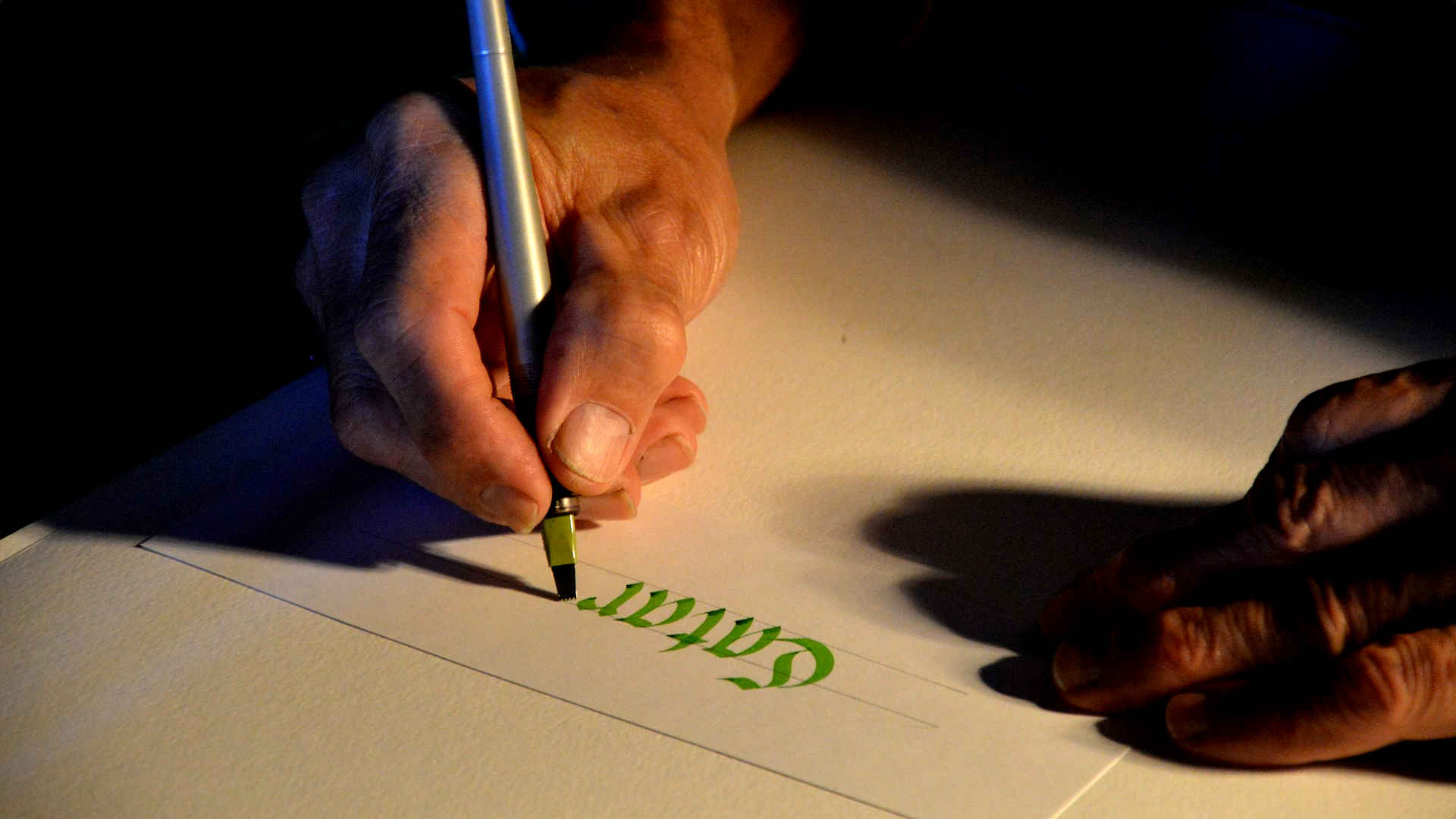 Wir beobachten einen Kalligrafen bei seiner Arbeit. Er benutzt einen grün schreibenden Stift mit einer flachen pinselartigen Spitze.