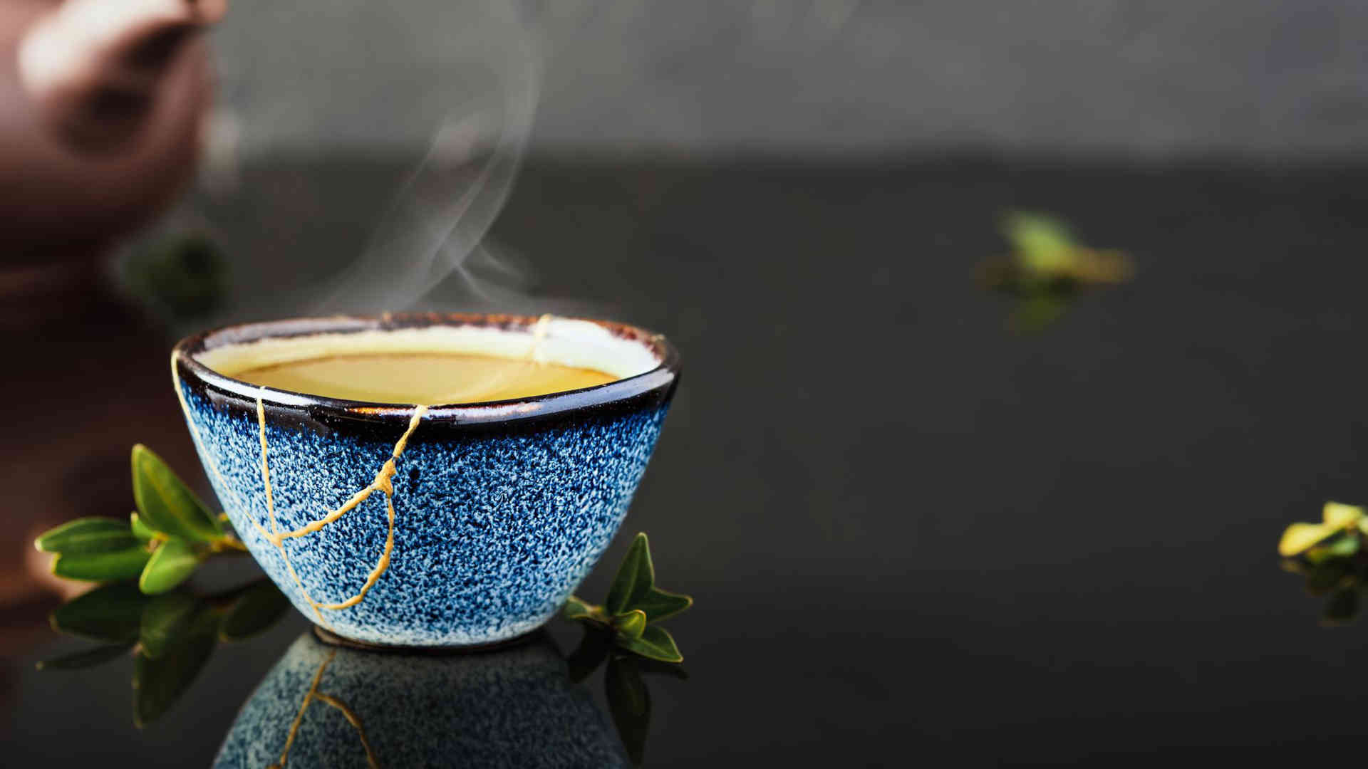 Eine Teeschale mit dampfenden Tee. Die goldenen Linien deuten darauf hin, dass sie mit Hilfe von Kintsugi wieder zusammengesetzt wurde. Sie hat damit ein zweites Leben erhalten.